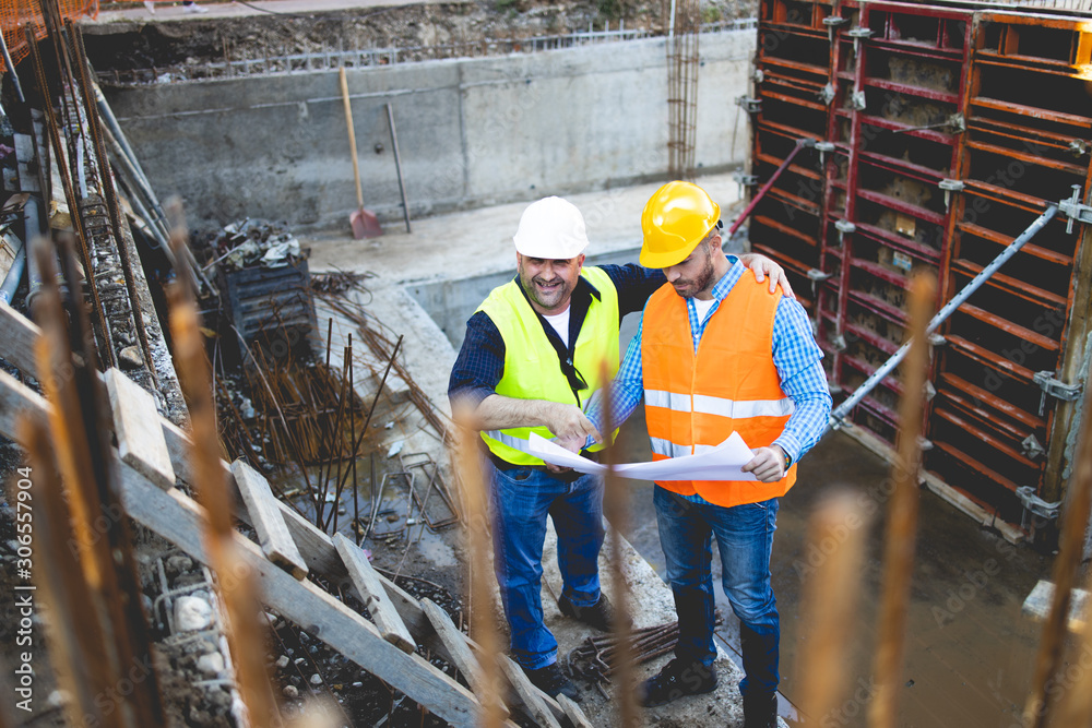 Men in hardhat and yellow and orange jacket posing on building site Men in hardhat and yellow and orange jacket posing on building site