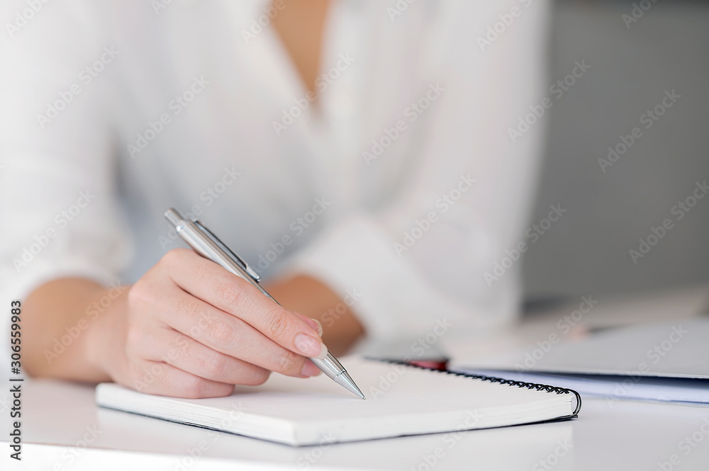 Close shot of a female hand writing something on notebook on the foreground. Close shot of a female hand writing something on notebook on the foreground.