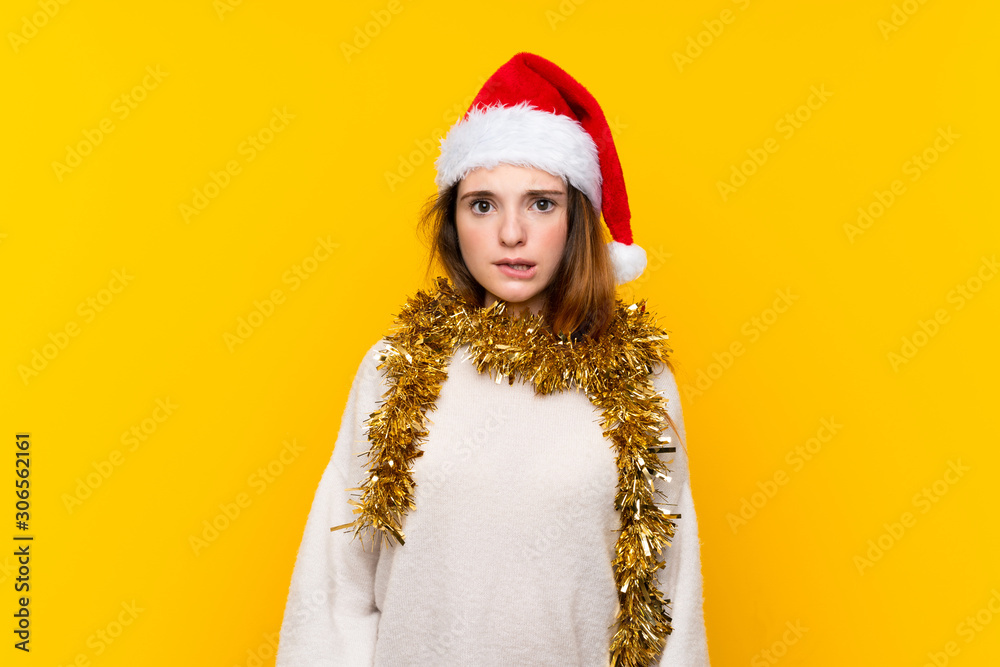 Girl with christmas hat over isolated yellow background having doubts and with confuse face expression Girl with christmas hat over isolated yellow background having doubts and with confuse face expression