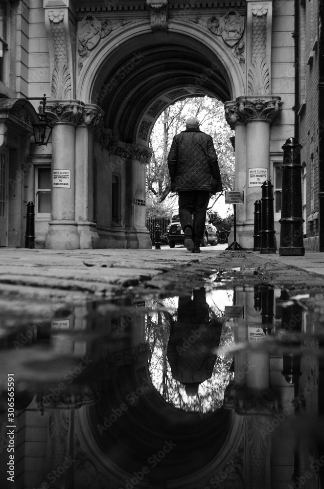 old man walks through an arch while his figure is reflected in the water