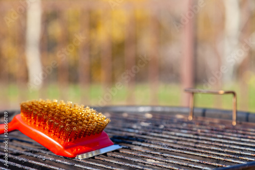 Photography Close-up of a red brush with golden bristles and a scraper for cleaning a barbecue grill grate