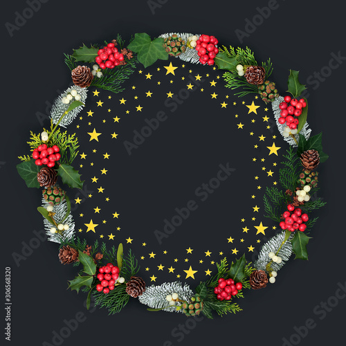 Fototapeta Naklejka Na Ścianę i Meble -  Gold star Christmas wreath with holly &  a variety of flora & winter greenery with loose stars on dark grey background with copy space.