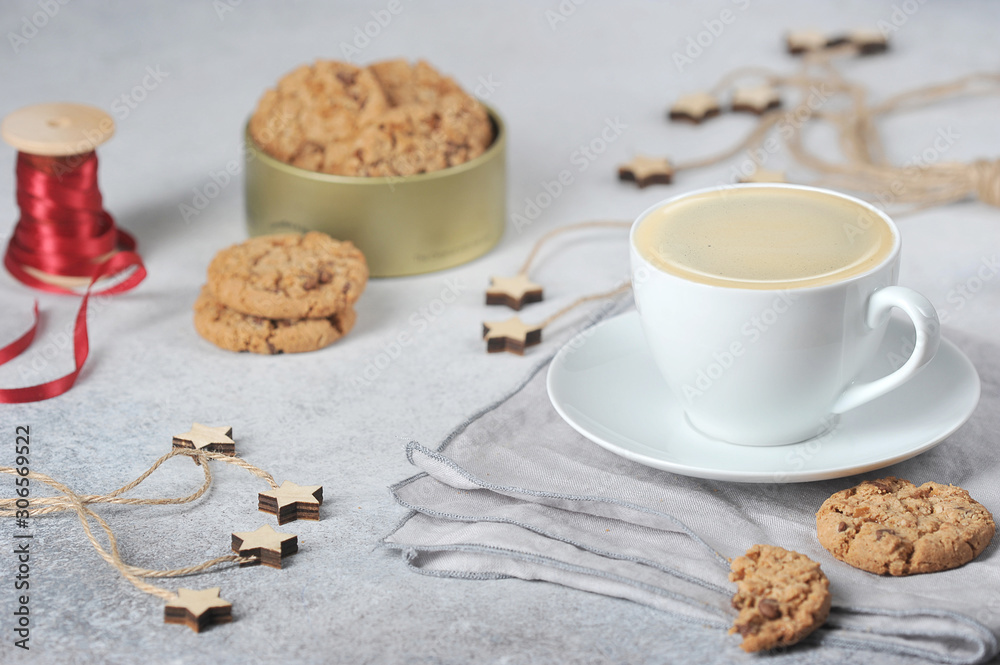 A cup of coffee and oatmeal cookies with pieces of chocolate. Red ribbon and decor create a festive mood concept. Light background.