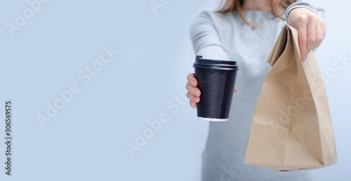 Woman holding cardboard cup of coffee and package food take and go in hand on gray light background