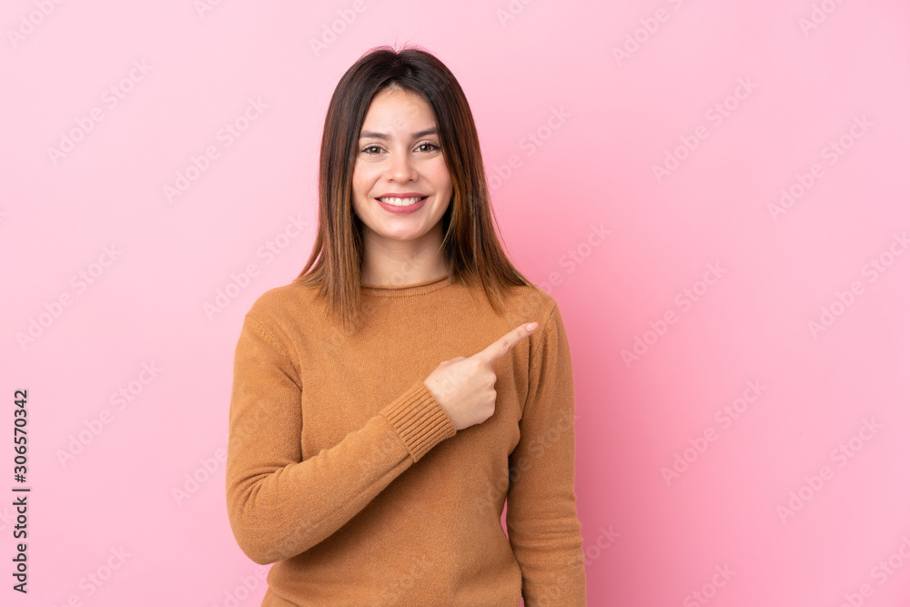 Young woman over isolated pink background pointing to the side to present a product Young woman over isolated pink background pointing to the side to present a product
