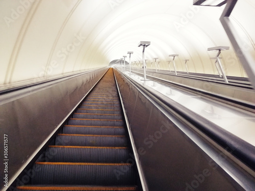 Descent into the tunnel stereo escalator stairs light from below. Modern tunnel escalator electronic system moving vintage style, Mechanical escalators for people up and down
