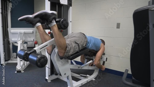 Man working out in gym exercising, strength training lifting weights doing leg exercises, leg curls on an exercise leg curl machine.