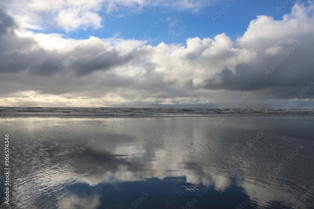 Ocean beach scene with white puffy clouds and blue sky reflecting on wet sand