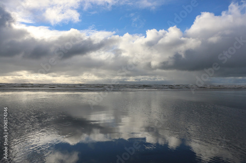 Ocean beach scene with white puffy clouds and blue sky reflecting on wet sand