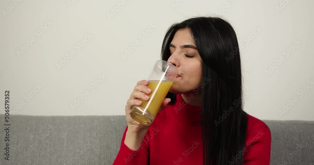 Brunette girl drink orange juice in the gray sofa . Deliciously Brunette girl drink orange juice in the gray sofa . Deliciously
