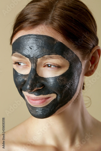 Charcoal face mask or black clay mud. Beautiful woman with black mask on her face, close up studio head shot. Natural cosmetic concept.