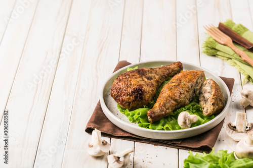 Fried chicken drumstick stuffed with mushrooms flat plate with lettuce leaf on light wooden background.
