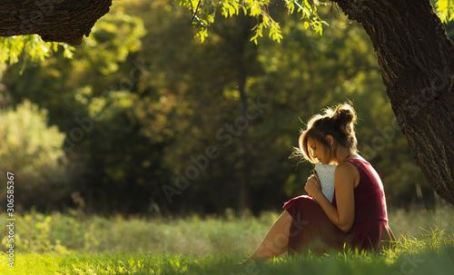 sunny portrait of a beautiful girl sitting on green glade under tree branches with book, woman reading novel on nature, concept hobby and lifestyle