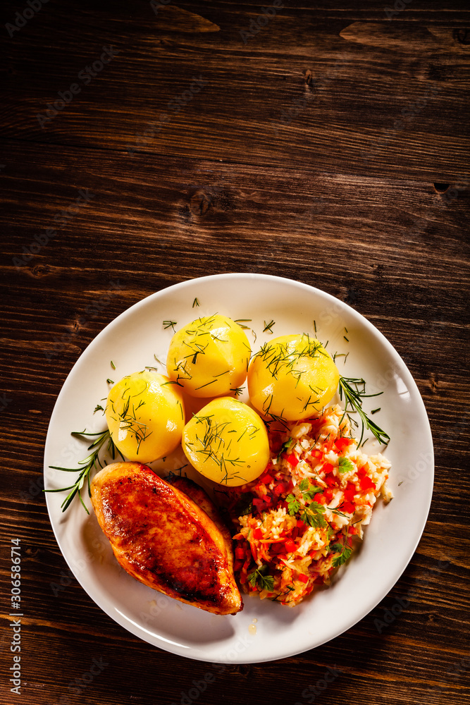 Fried chicken breast with boiled potatoes and vegetables on timber background