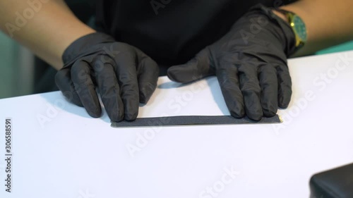 Closeup view of hands of professional manicurist wearing black gloves and prepars sterile tools for making nail manicure in beauty salon. Woman applies disposable emery sticker to nail file board photo