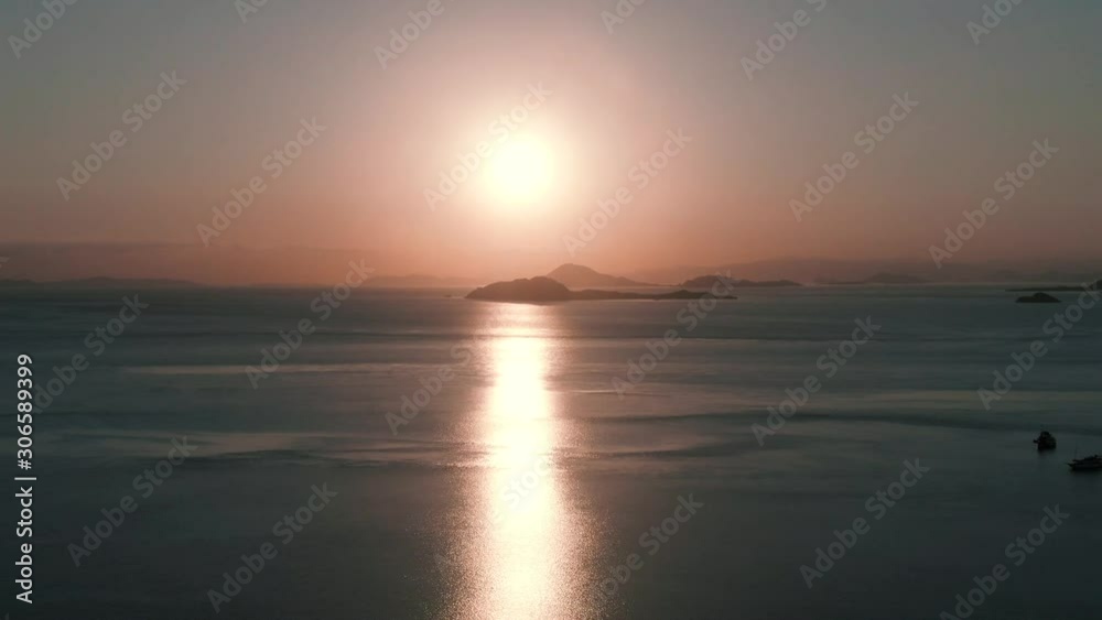 Sinking drone shot of beautiful sunrise with small islands in the background and reflection on water Sinking drone shot of beautiful sunrise with small islands in the background and reflection on water