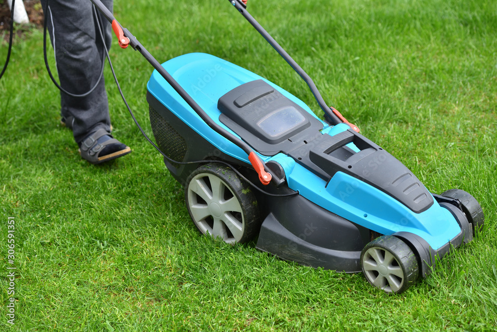 Electric lawn mower mows a bright green overgrown lawn, close-up Electric lawn mower mows a bright green overgrown lawn, close-up