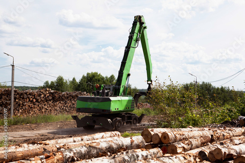 A reloader (excavator) in the open warehouse of logs for a plywood factory