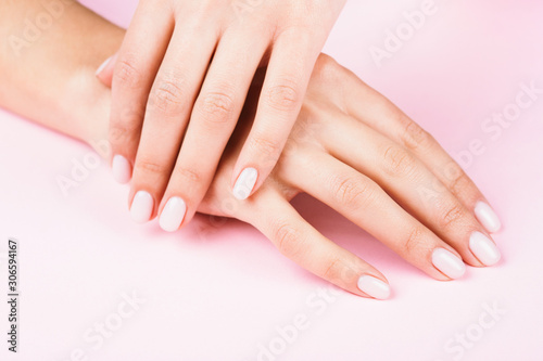 Female's hands with classic pastel manicure on pink background. Beauty salon.