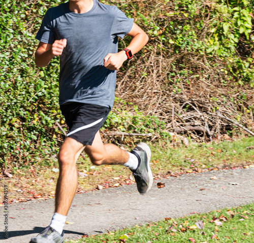 One boy running next to green busches on tar path in park photo