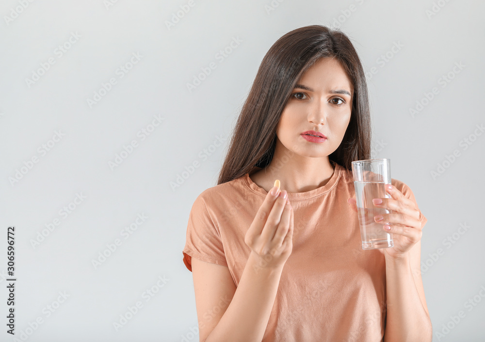 Young woman taking pill on light background Young woman taking pill on light background