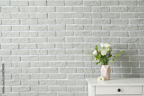 Fresh flowers in vase on table near brick wall