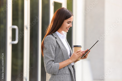 Beautiful young businesswoman with coffee and tablet computer outdoors