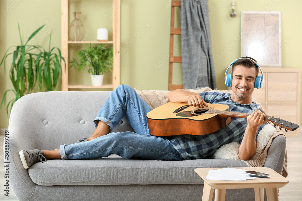 Obraz premium Handsome man with guitar listening to music at home