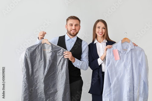 Workers of modern dry-cleaner's with clothes on light background