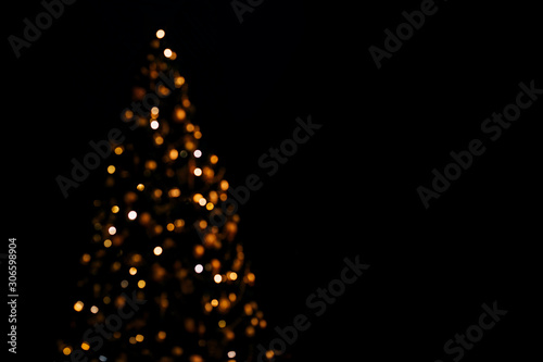 Lights of christmas tree blurred bokeh on dark background with copy space.