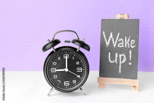 Alarm clock and chalkboard with text WAKE UP on table photo