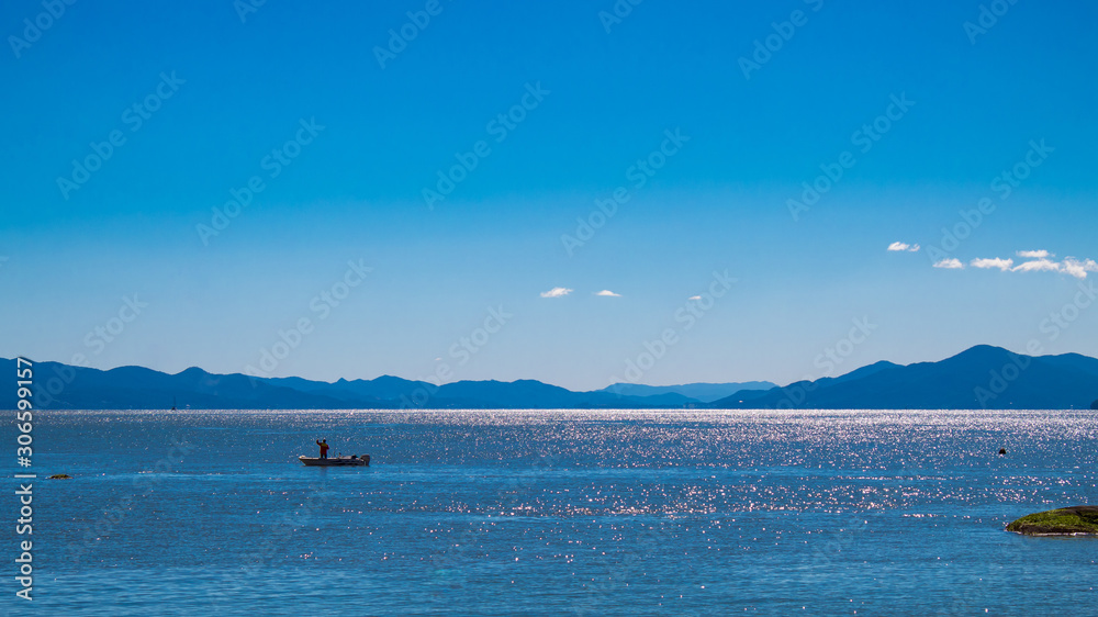  Mar azul tropical em dia de sol, pedras e barco de pesca no fundo montanhas azuis