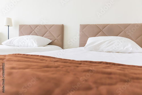 European light bedroom interior with brown, beige cozy bed and white linen, and brown bedspread