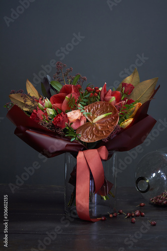 Chic autumn bouquet in red colors in vintage style in a glass vase and a huge jar of dry rose hips on a dark background, selective focus