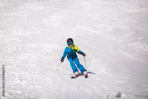 Little girl in blue and yellow ski costume skiing in downhill slope. Winter sport recreational activity
