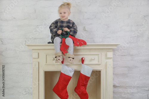 Adorable toddler girl sitting on top of wooden fireplace decorated with red Christmas socks, winter holidays at home photo