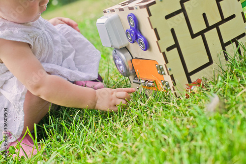 Cute little girl is playing with busiboard outdoors on green grass. Educational toy for toddlers. girl opened door to cube of board.
