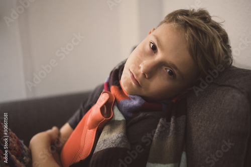 Canvas Print Sick boy sitting with woolen blanket and hot water bottle