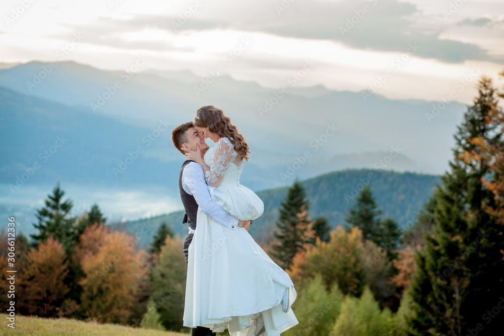Beautiful wedding couple, bride and groom, in love on the background of mountains. The groom in a beautiful suit and the bride in a white luxury dress. Wedding couple is walking Beautiful wedding couple, bride and groom, in love on the background of mountains. The groom in a beautiful suit and the bride in a white luxury dress. Wedding couple is walking