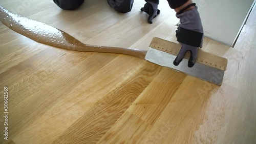 Carpenter master with gloves grouting wooden parquet, phase after sanding. Varnishing of oak parquet floor, man workers with hand and spatula