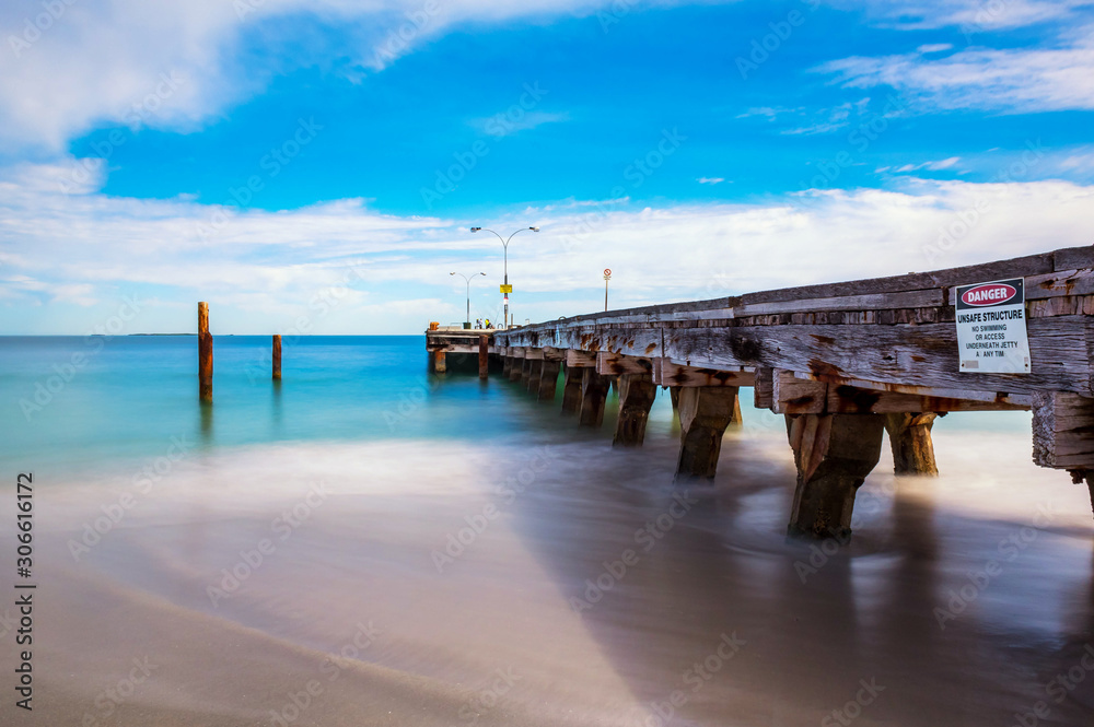 Obraz premium Long exposure, blue sky, moving water, beach, fishermen on jetty 
