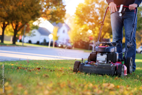 Mowing the grass with a lawn mower in sunny autumn. Gardener cuts the lawn in the garden photo