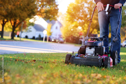Mowing the grass with a lawn mower in sunny autumn. Gardener cuts the lawn in the garden