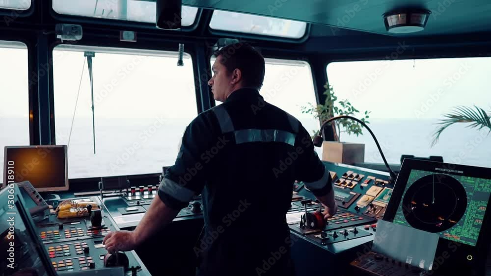 Marine navigational officer during navigational watch on Bridge . He is maneuvering the ship. Work at sea.