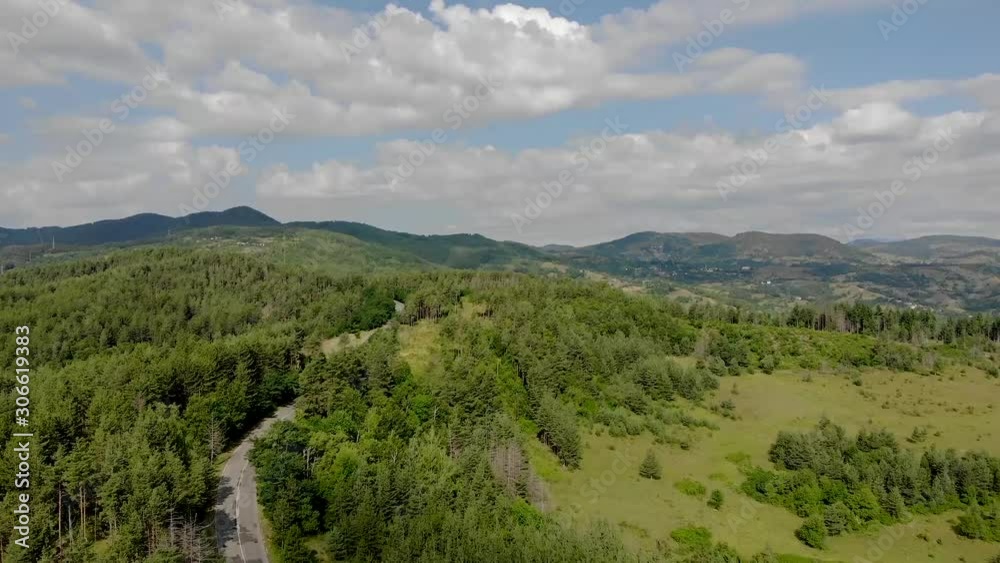 Flying over an empty road surrounded by trees in the mountains with clouds in the sky Flying over an empty road surrounded by trees in the mountains with clouds in the sky