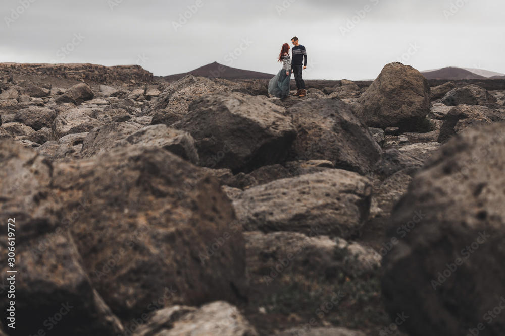 Couple in love walking in Iceland. Stone volcanic desert around, in the middle of nowhere. Dramatic nordic landscape, cold weather. Wearing in traditional wool sweaters, jeans and gray skirt.