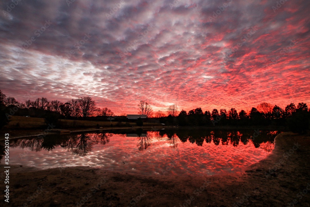 Naklejka premium Dramatic red sunrise clouds over a tranquil country pond 