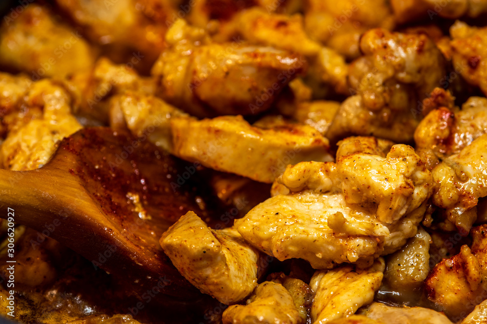 Marinated torn cut chicken bits being cooked, halfway cooked. Spicy chicken, wooden spatula