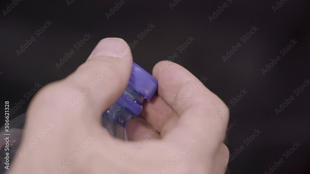 Hands open the blue cap of a bottle of fresh water on a dark background. Hands open the blue cap of a bottle of fresh water on a dark background.