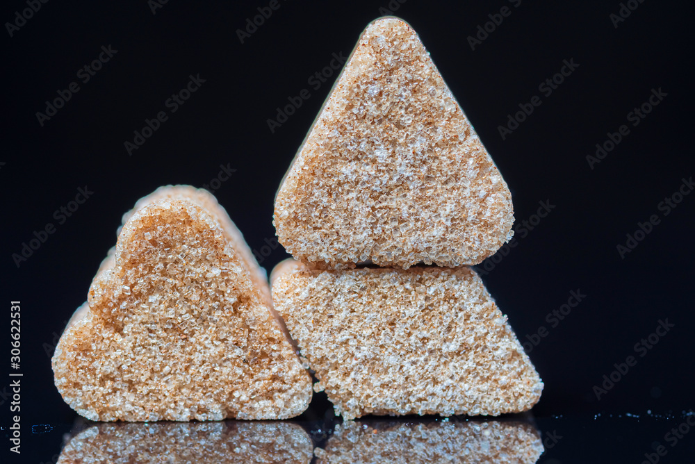 A piece of refined sugar with cinnamon on a black background. Photographed close-up. A piece of refined sugar with cinnamon on a black background. Photographed close-up.